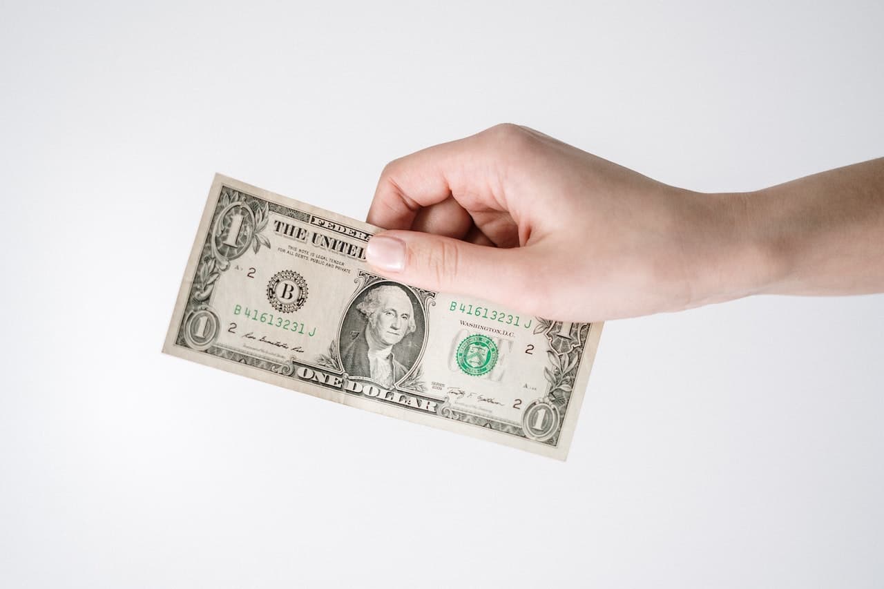 Woman's Hand Holding One Dollar Bill With A White Background