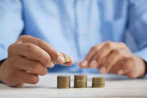 man's hand adding a coin on top of a pile of coins